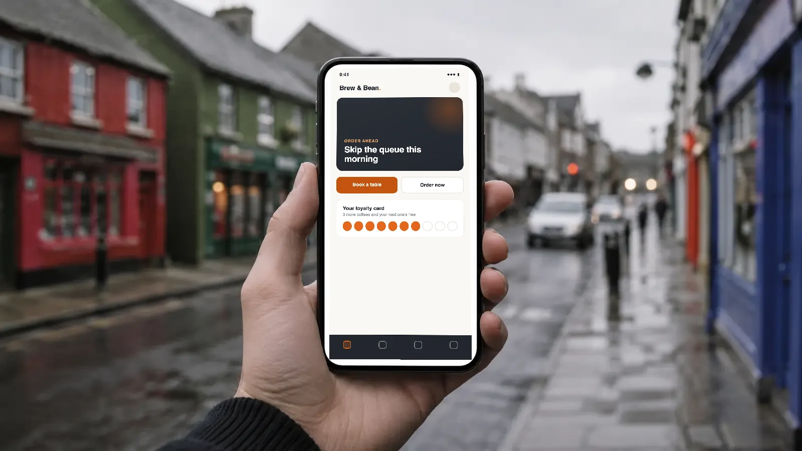 A hand holding a phone showing a business app, on a colourful Irish high street